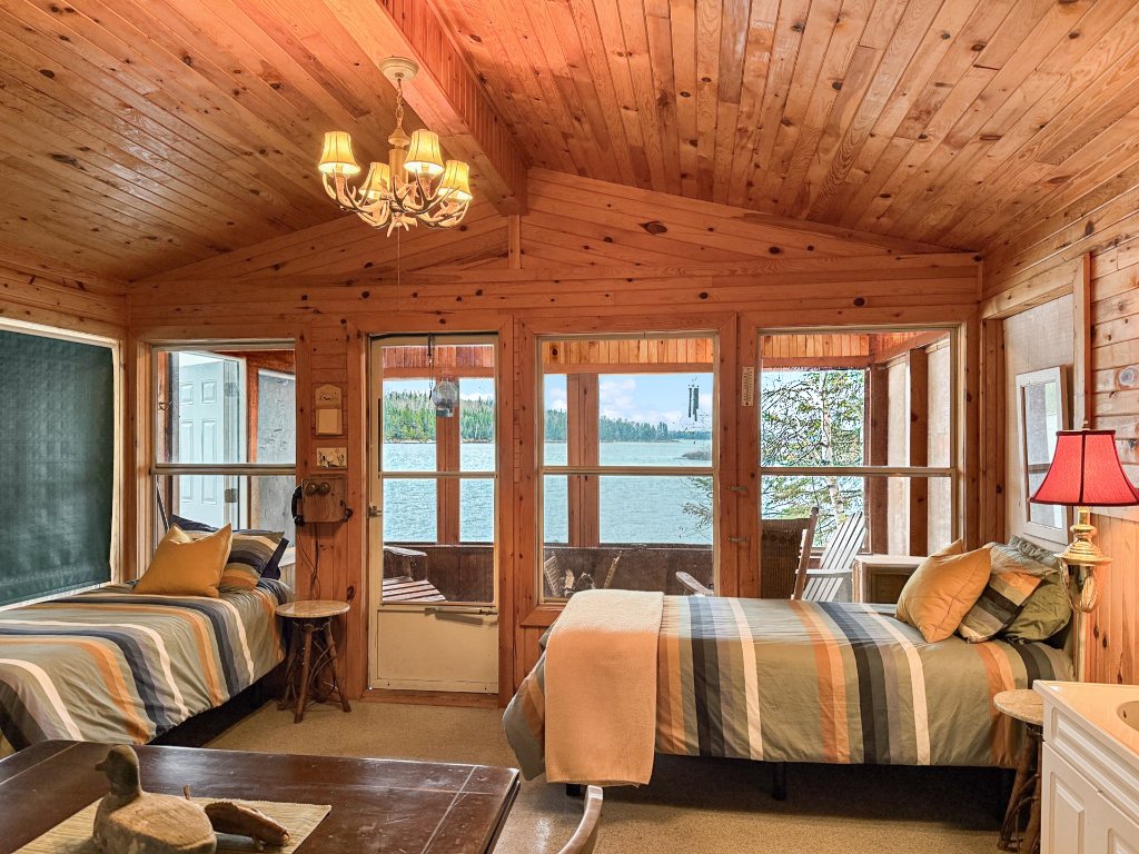 The bunky interior at Kendall's Point — two striped-quilt beds in a warm cedar-lined room with lake views through the windows