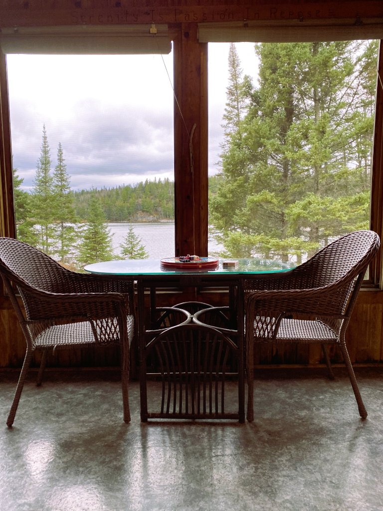 Wicker chairs and a table in the cottage screen room with a lake view
