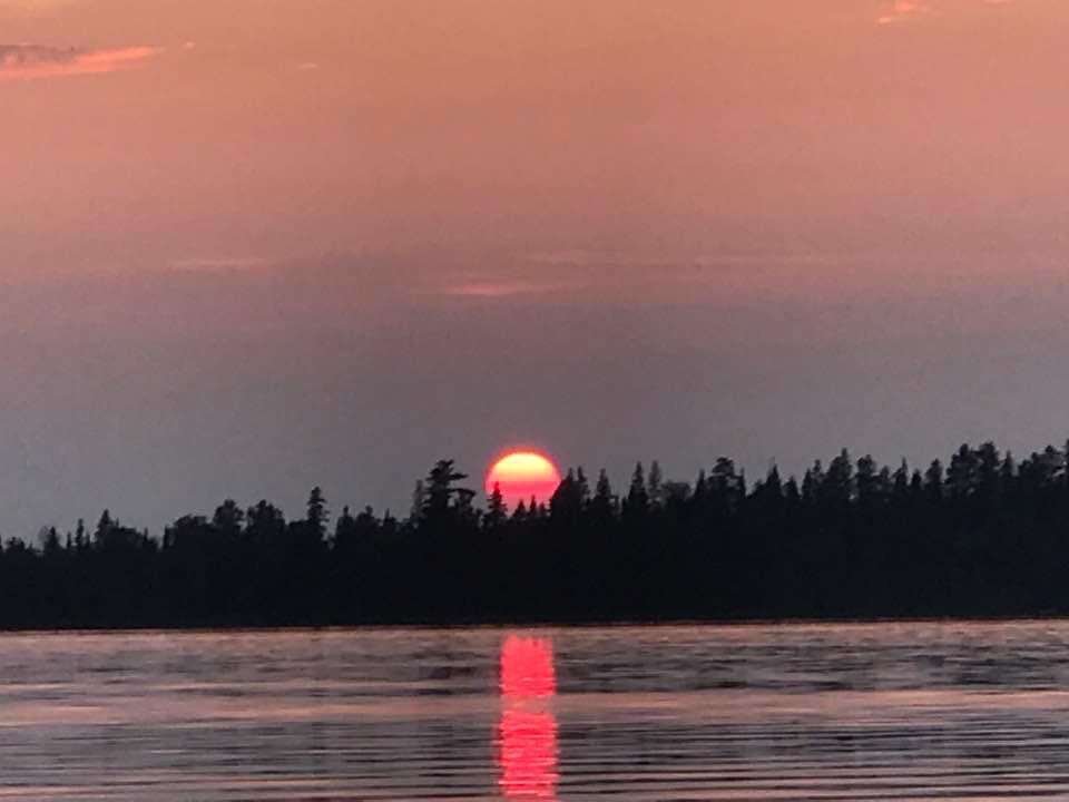Red sun setting over the treeline and reflecting on Gunn Lake