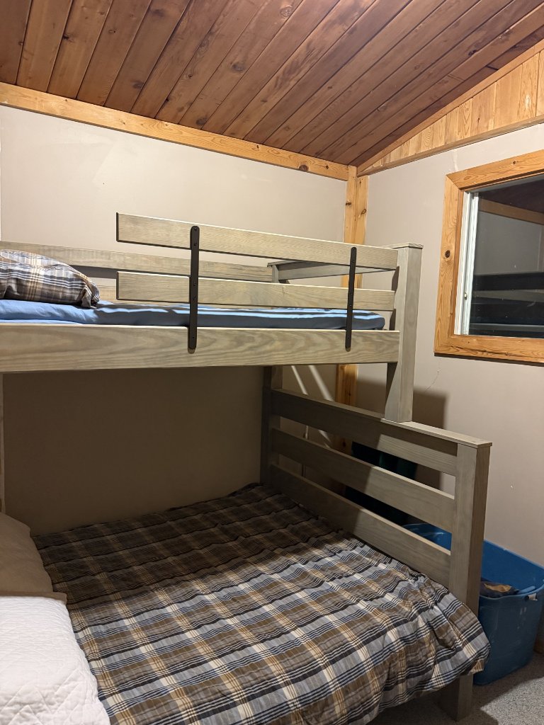 Cottage bedroom with grey bunk beds and plaid bedding under a wood ceiling
