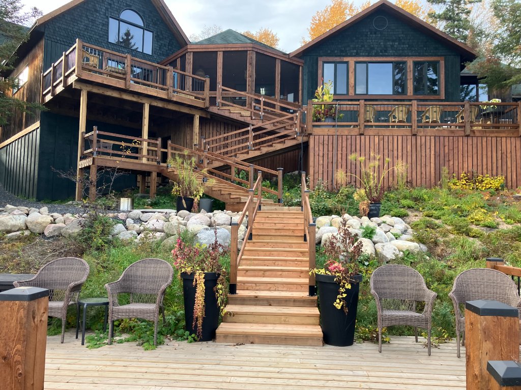 Front view of Gunn Lake Lodge — dark shingled cabins with cedar decks and a boardwalk against a summer sky