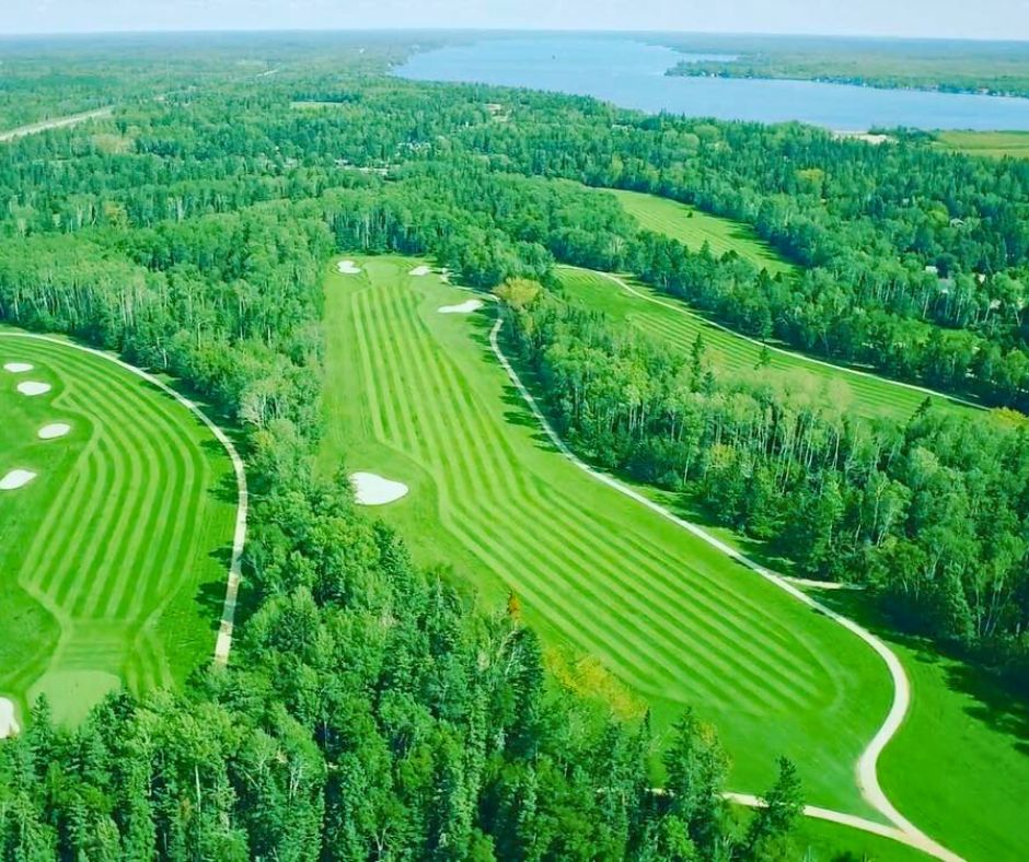 Aerial view of a golf course fairway winding through boreal forest at golden hour