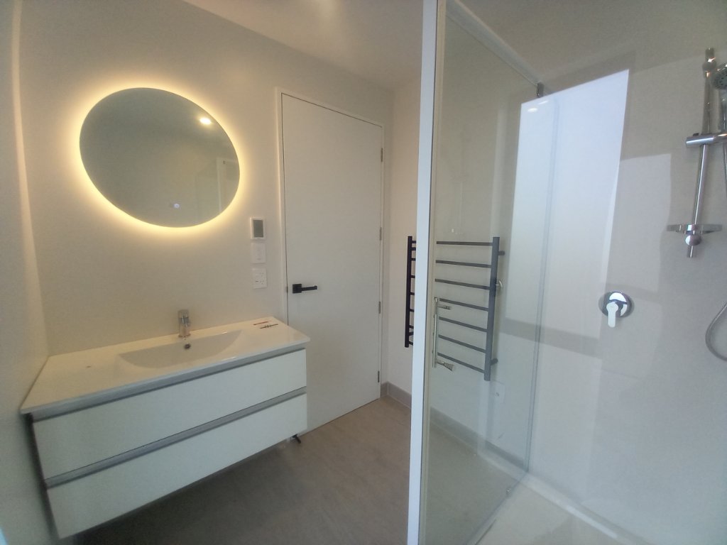 Bathroom with backlit round mirror and glass shower
