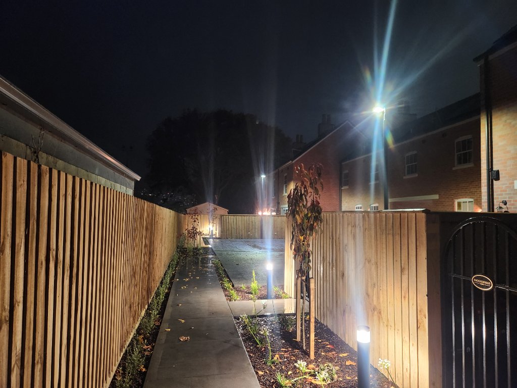 Fenced pathway with bollard and garden lighting at night