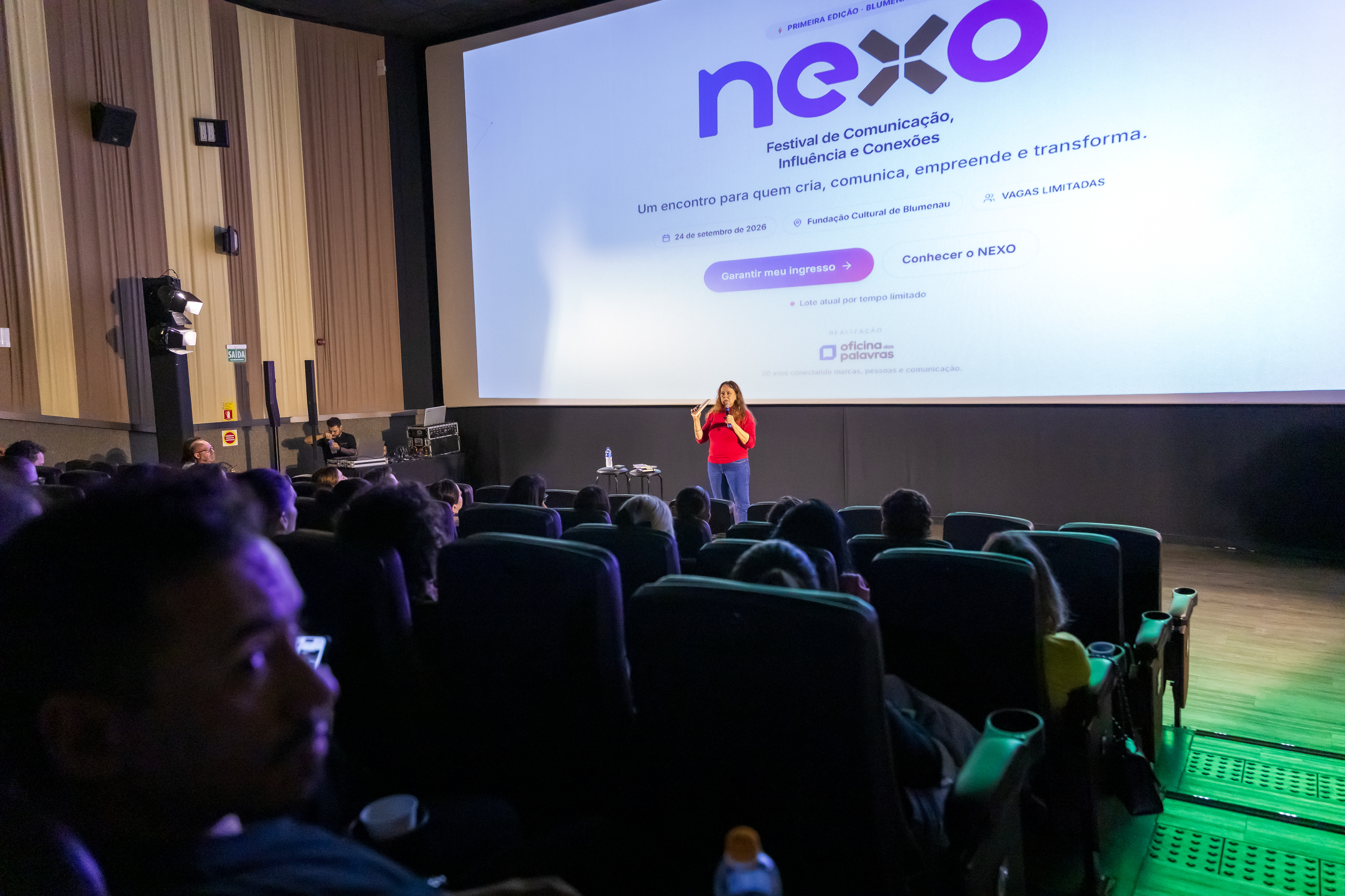 Palco com a identidade do NEXO projetada, palestrante e plateia no lançamento