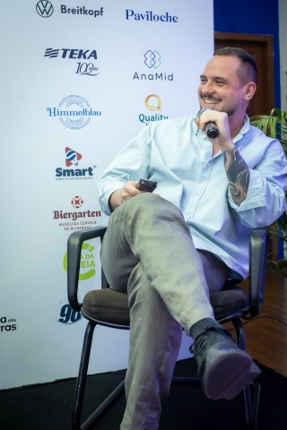 Palestrante masculino sorrindo no palco do NEXO