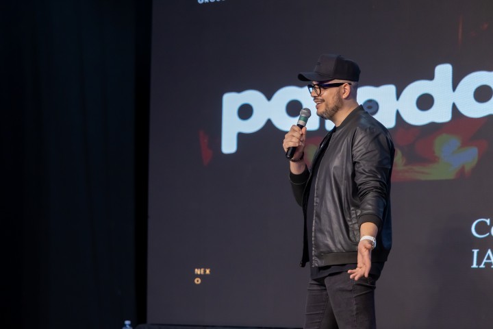 Palestrante com boné preto no palco do NEXO 2026