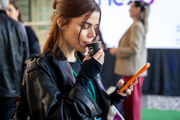 Participante com café e celular no NEXO 2026