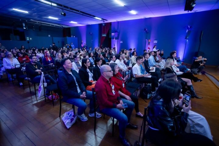 Público no auditório do NEXO 2026 com iluminação azul e roxa