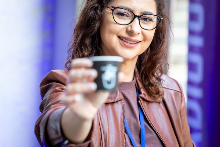 Participante erguendo copo de café no NEXO 2026