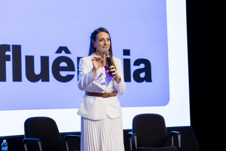 Palestrante no palco com tela de fundo no NEXO 2026