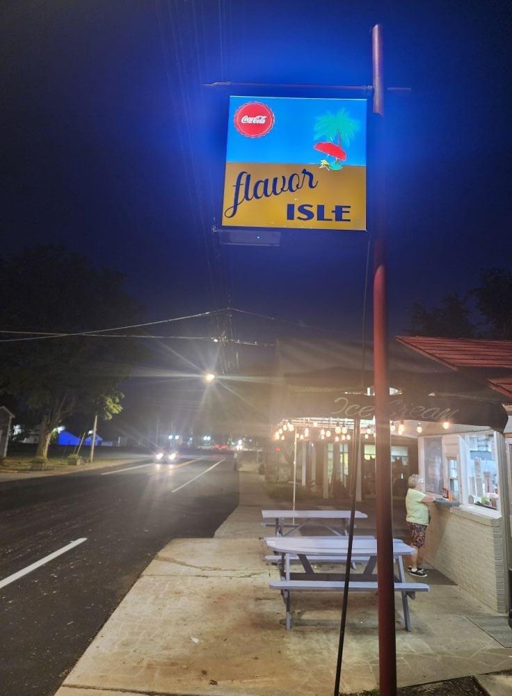 Flavor Isle sign glowing at night over the picnic tables