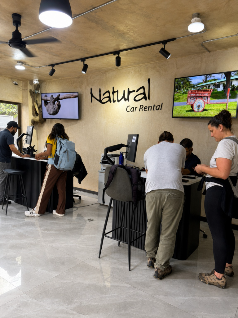 Customers with luggage receiving assistance at the Natural Car Rental counter.