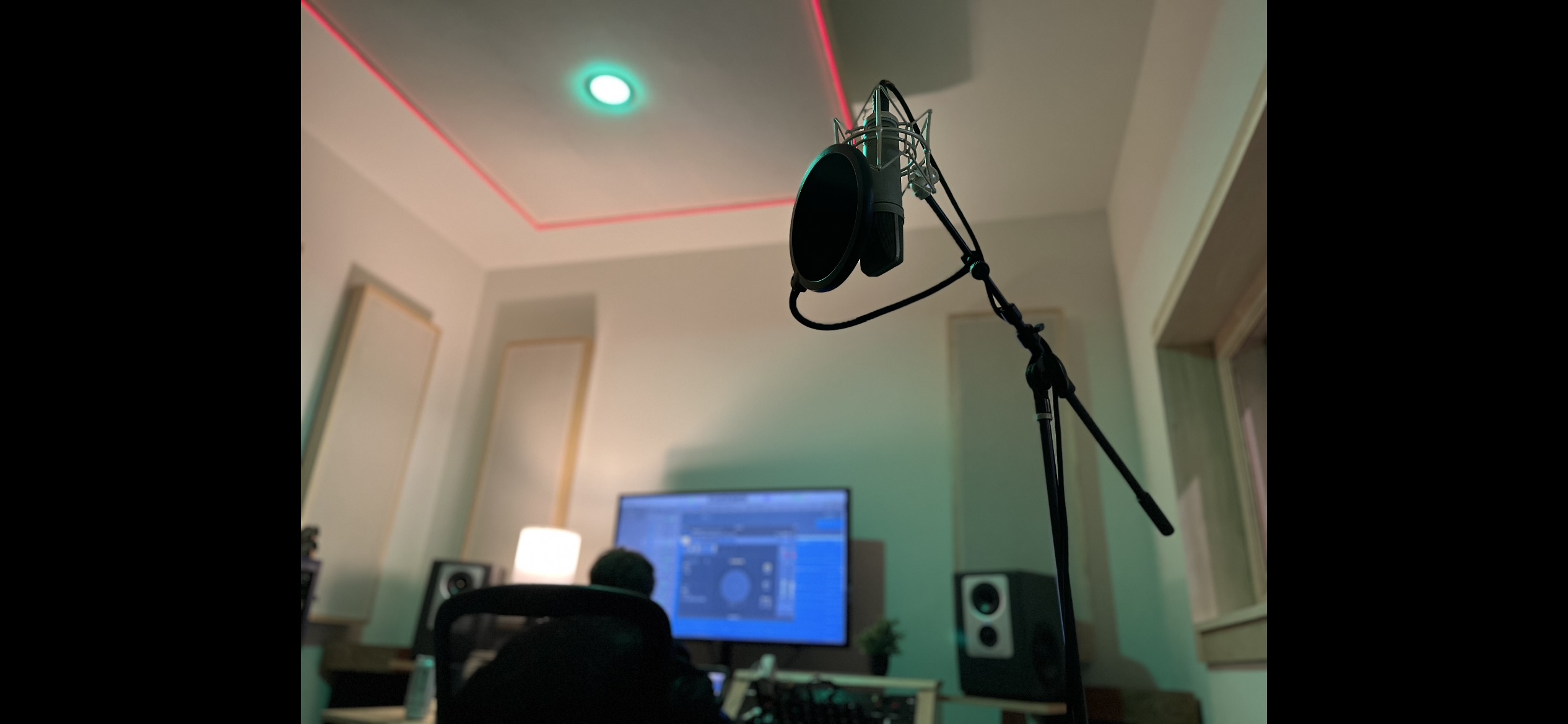 Large-diaphragm condenser microphone on a shock mount with pop filter, lit by green ambient studio light