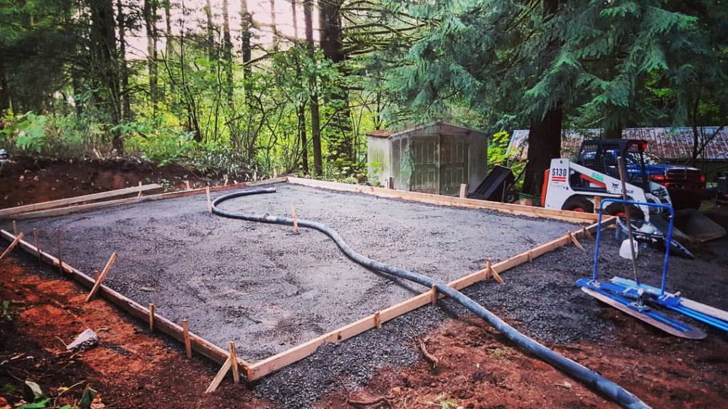 Concrete foundation pour with pump hose and skid-steer in wooded setting