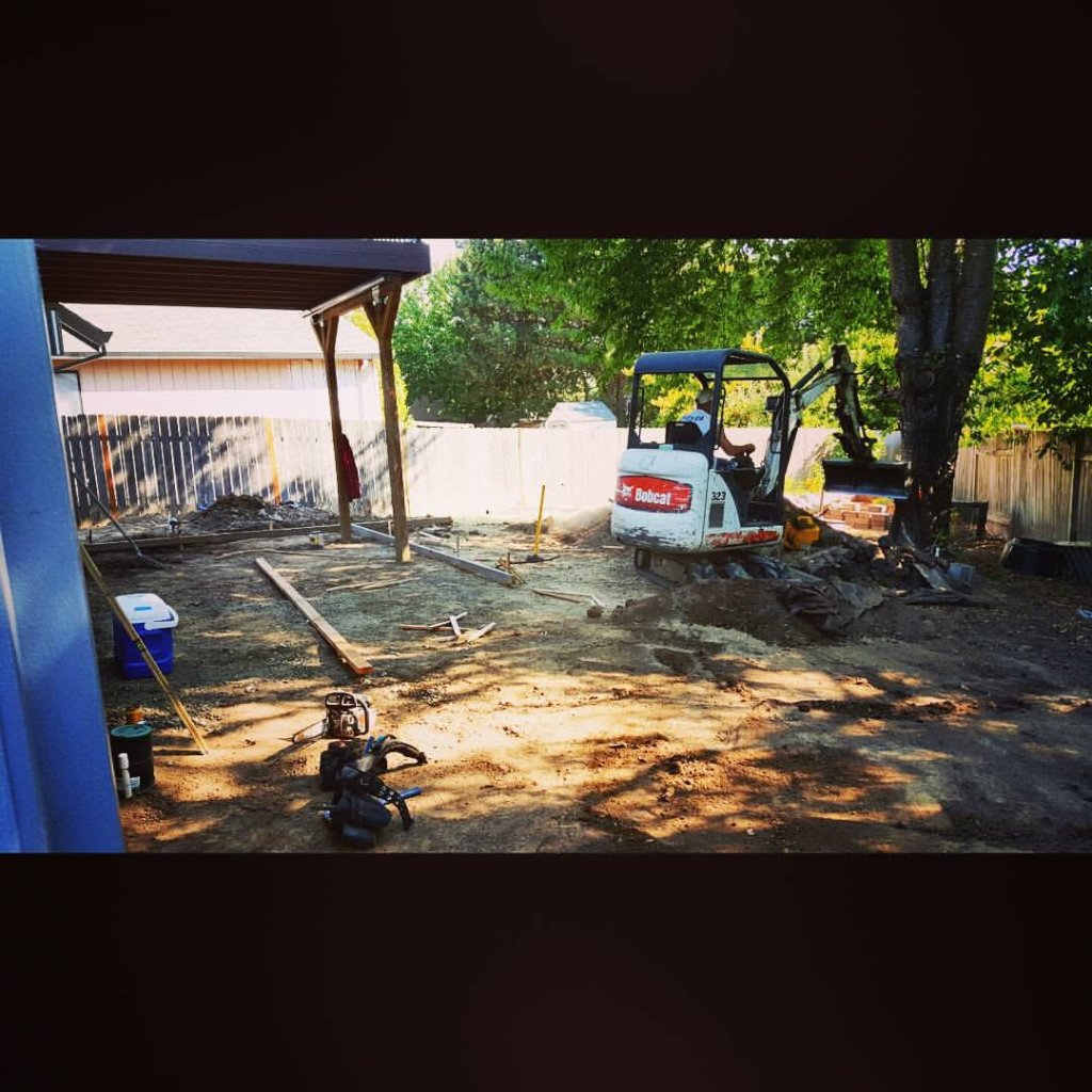 Mini-excavator grading backyard site for concrete patio installation