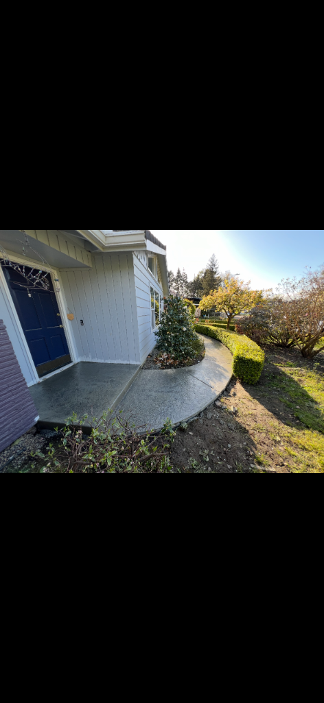 Finished light-gray stamped concrete walkway curving along the side of a residential home toward the front entrance