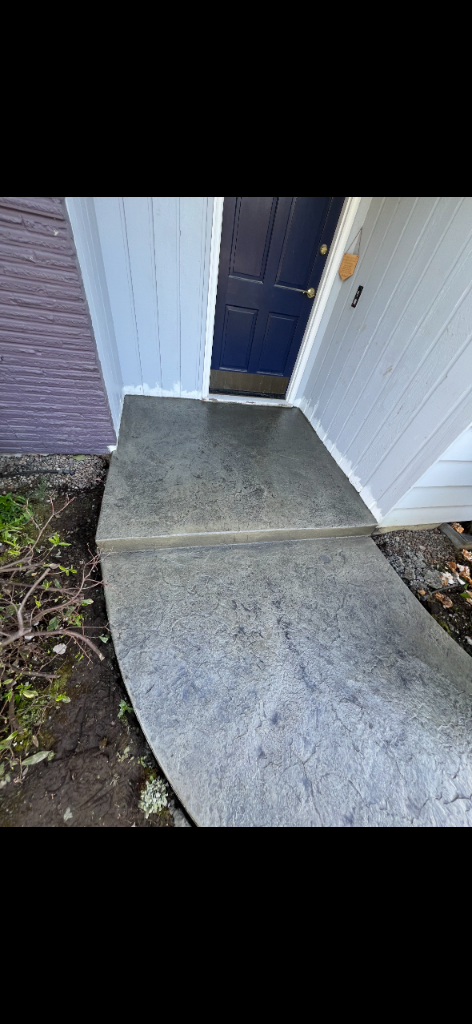 Finished stamped concrete walkway curving up to a navy blue front door with a rectangular entry landing