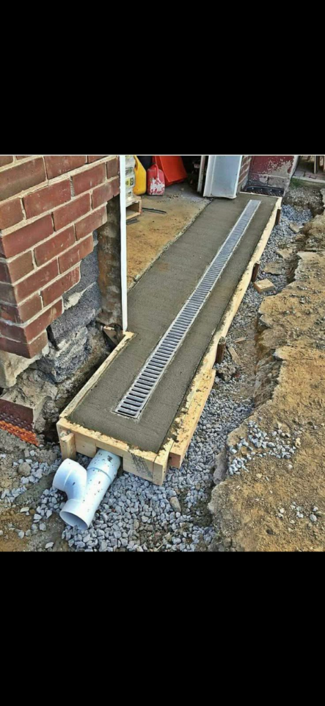 Linear trench drain set in formwork with PVC pipe tied into an excavated trench