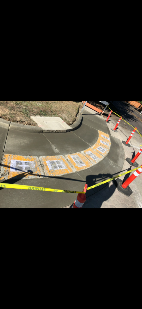 Completed ADA concrete curb ramp with yellow tactile warning surface and control joints, taped off while curing