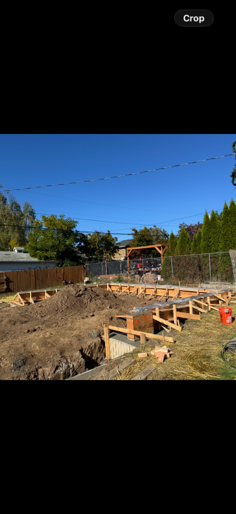 Excavated dirt and wooden concrete formwork staked in a backyard
