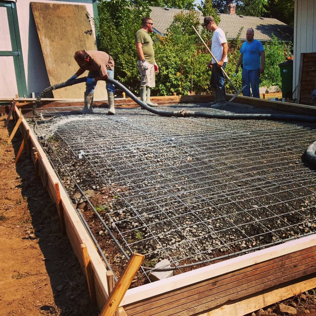 Concrete crew pouring a driveway with pump hose and wire mesh grid