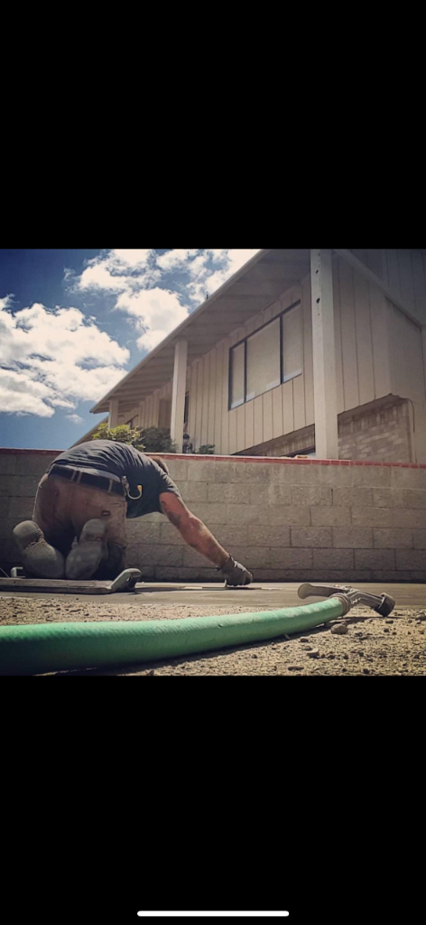Worker hand-finishing a wet concrete slab with a hand tool beside a block retaining wall