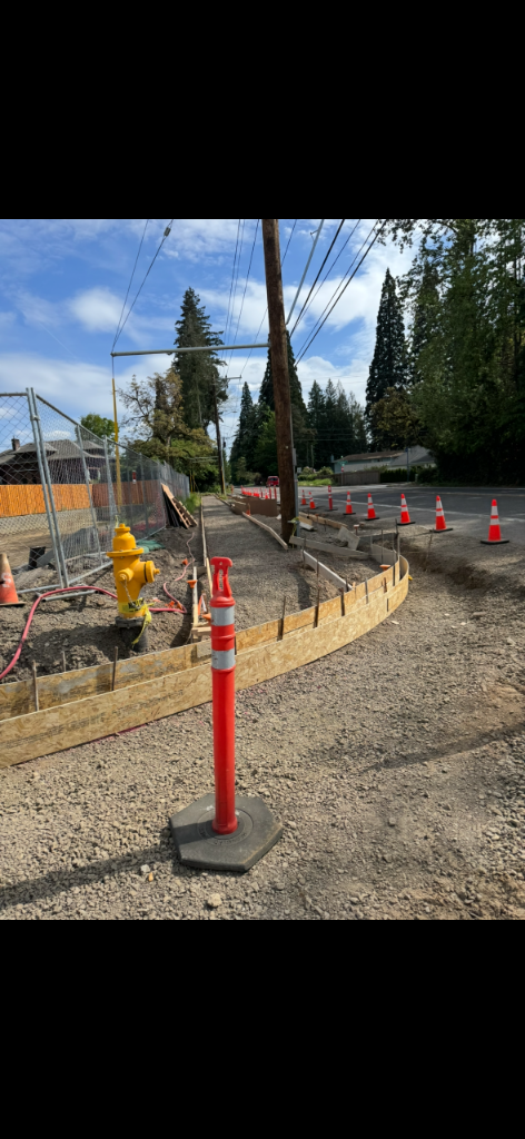 Curved wooden formwork staked along a future ADA curb ramp and sidewalk path over graded gravel