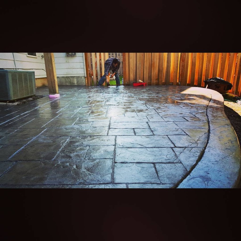 Dark grey slate-textured stamped concrete backyard patio with sealed glossy finish