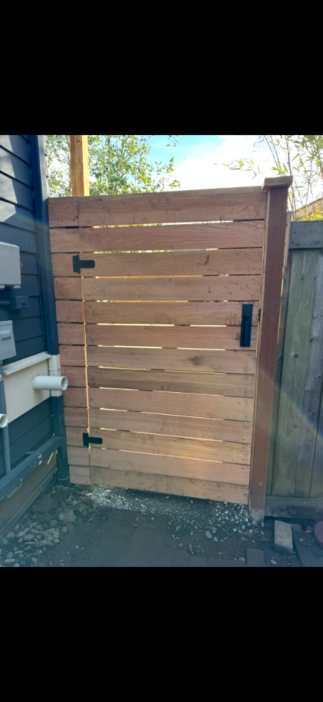Completed horizontal-slat cedar pedestrian gate installed beside a dark house exterior