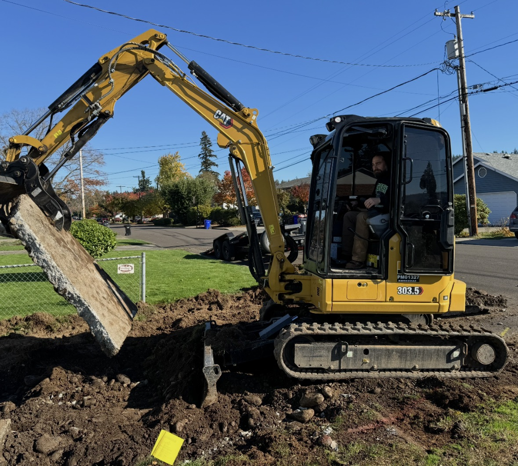 CAT mini-excavator bucket lifting a large broken concrete slab during driveway removal