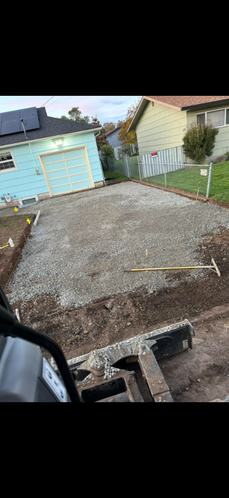 Leveled crushed-gravel patio base with string lines viewed from the excavator, prepared for a concrete pour