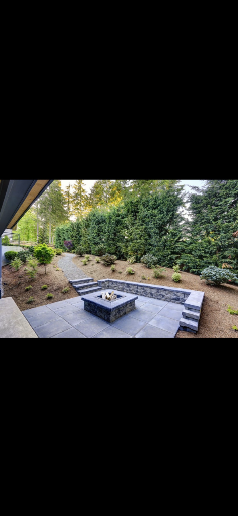 Completed fire pit set in a stone paver patio with a curved retaining wall and integral steps up the slope