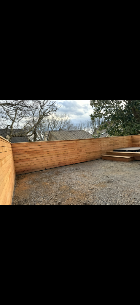 Completed L-shaped horizontal-slat cedar fence enclosing a yard corner over gravel ground