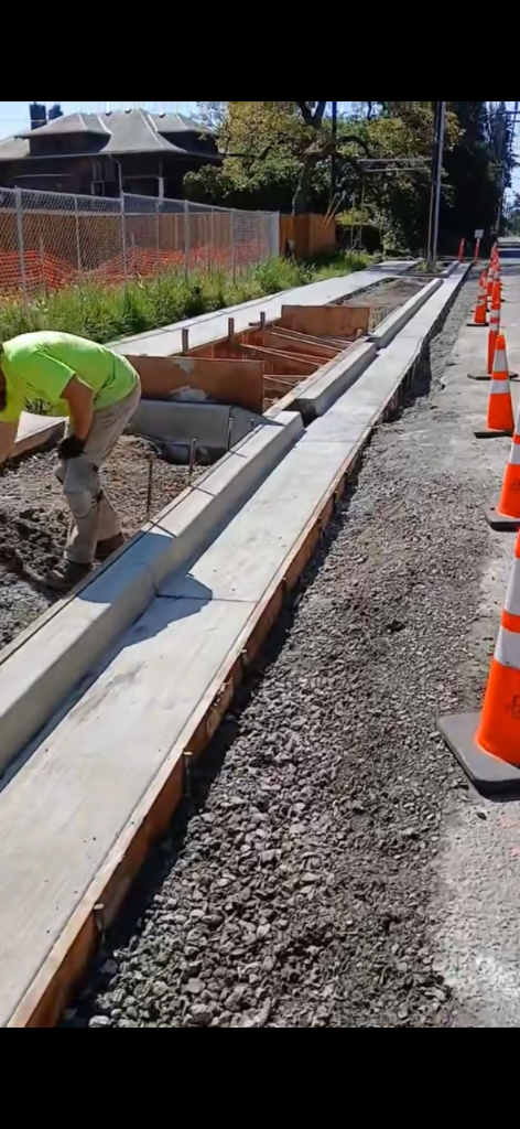 Worker setting wooden curb forms lined with traffic cones along the construction zone
