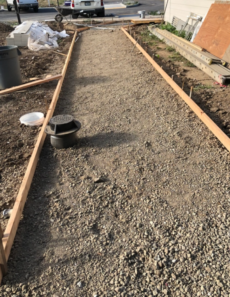 Narrow gravel pathway lined with wooden formwork and staked boards, prepared for a concrete pour