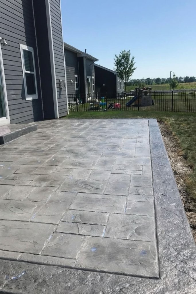 Completed stamped flagstone concrete patio in grey tones behind a residential home