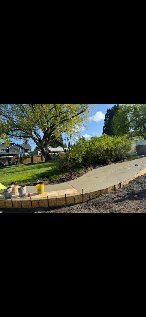 Newly poured concrete sidewalk ramp following a curved path with wooden formwork and expansion joints
