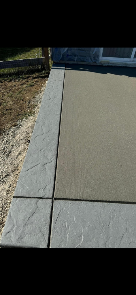 Dual-texture concrete patio with smooth grey center and stamped stone border