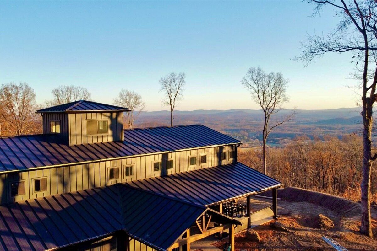 Hilltower home with standing-seam metal roof and tower overlooking a mountain valley at sunset