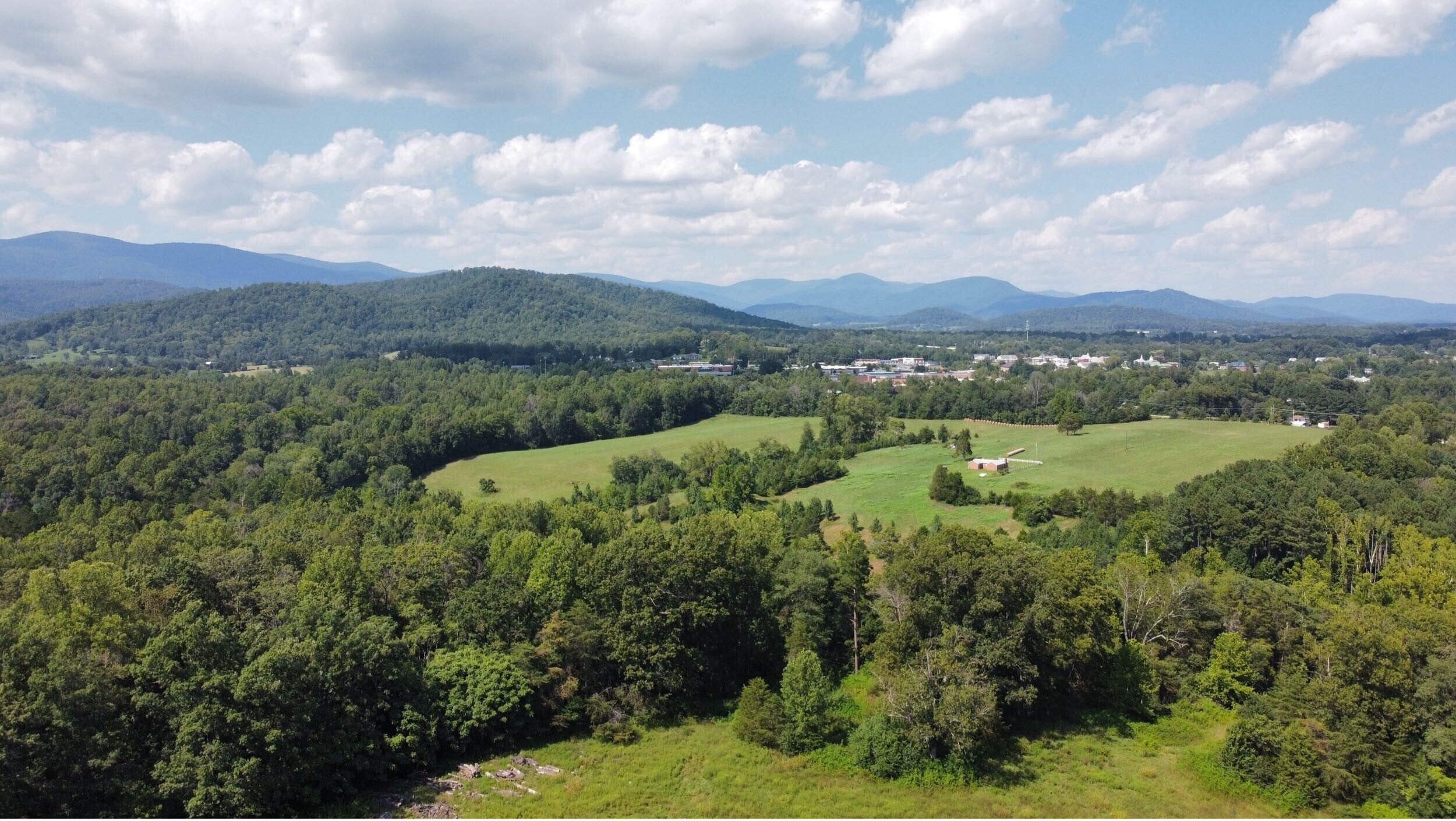 Aerial drone view of rolling Central Virginia land with open fields, forest, and Blue Ridge mountains