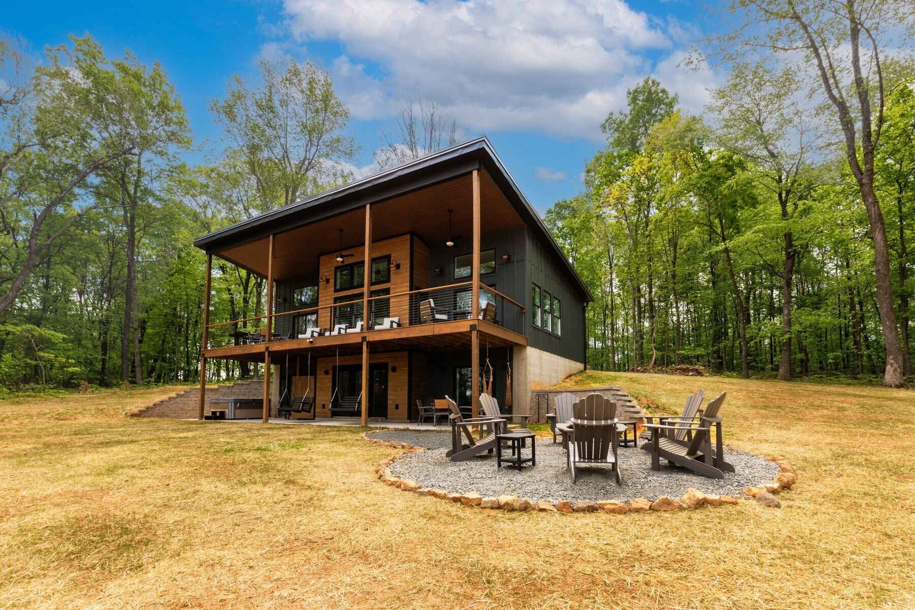 The Peak, a modern Bailey Builds home with a shed roof, wood-clad covered deck, and stone fire pit in a wooded clearing