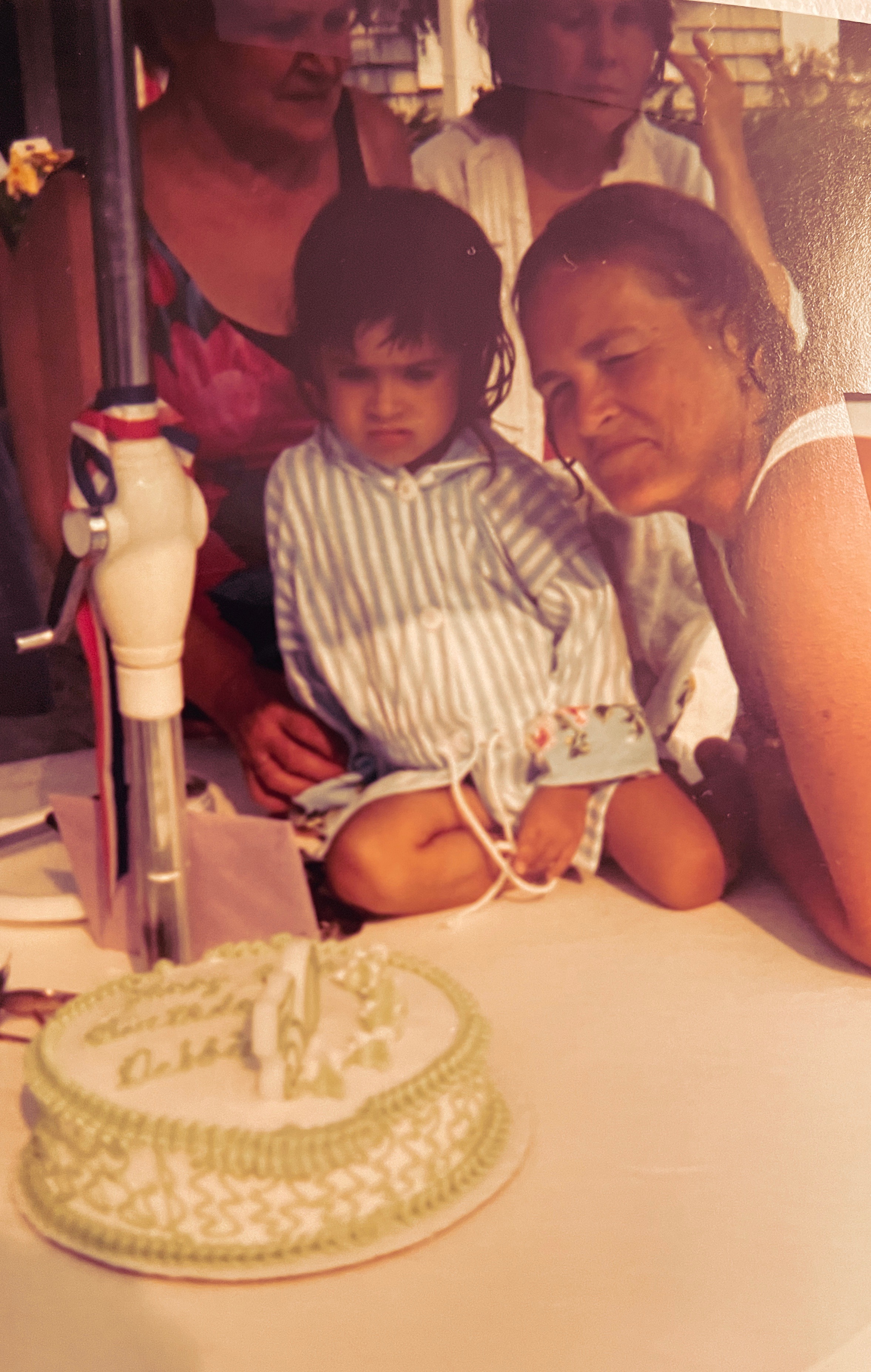 A warm vintage photograph of a child's birthday celebration, gathered around a cake with family