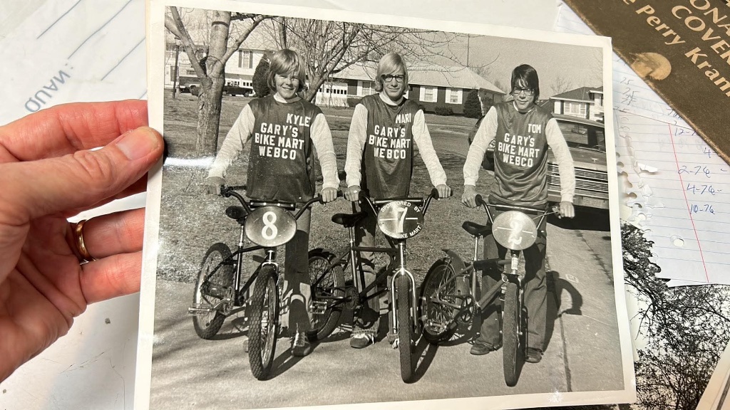 A hand holding the Gary's Bike Mart team photograph, surrounded by research papers and prints