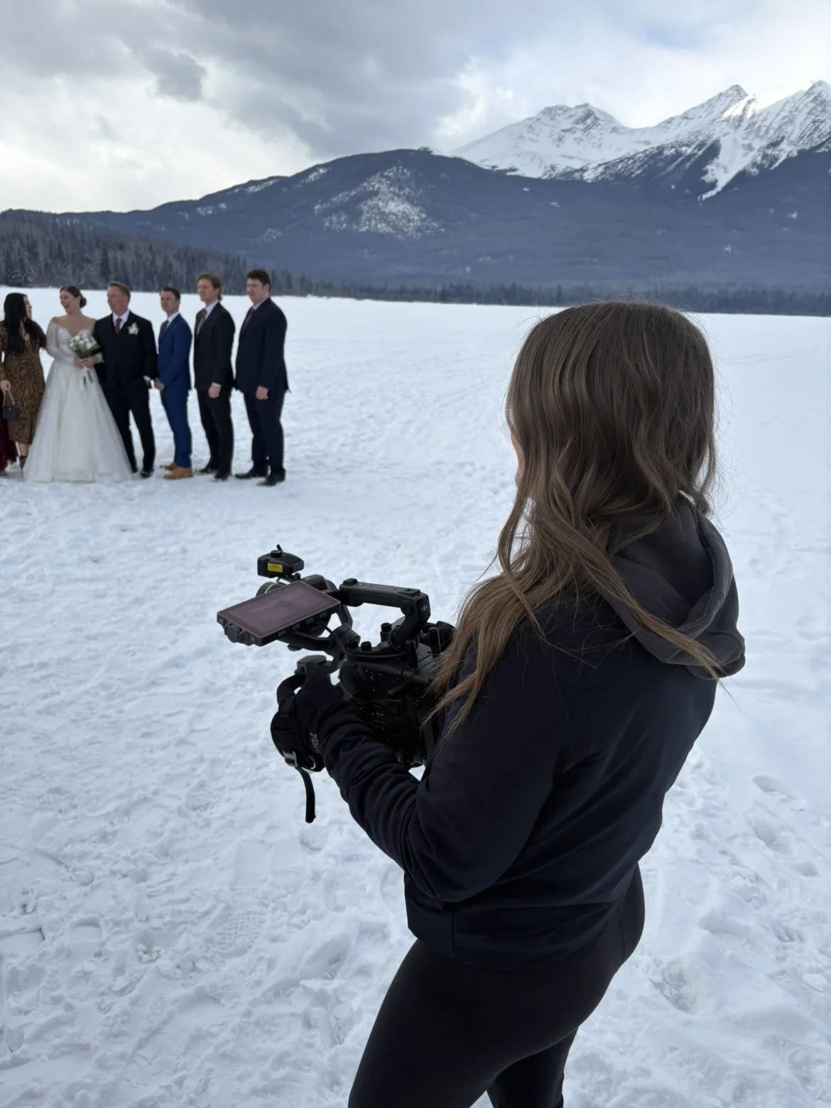 Taylor filming a wedding party in the snow with mountains behind