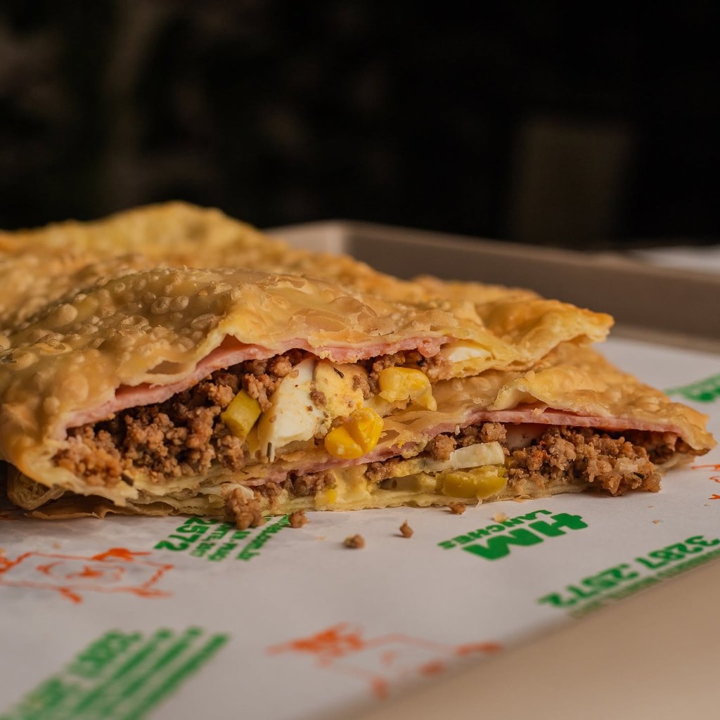 Pastel partido com carne moída, ovo cozido, milho e presunto