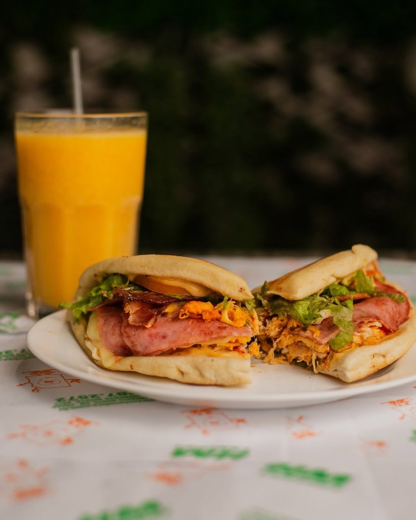 Sanduíche cortado ao meio com suco de laranja ao fundo