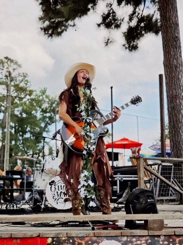 Camryn Marie performing outdoors with guitar and floral mic stand