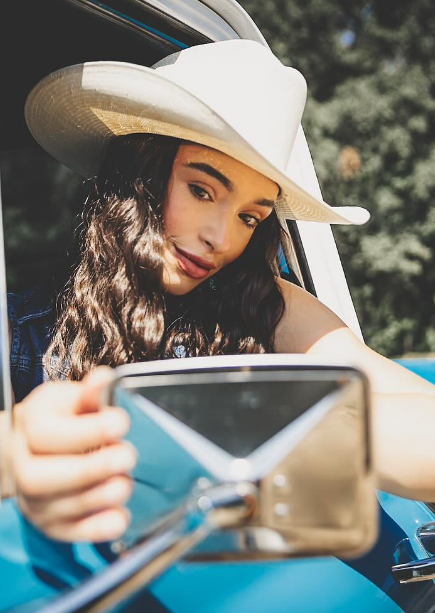 Camryn Marie in a cowboy hat through a truck side mirror