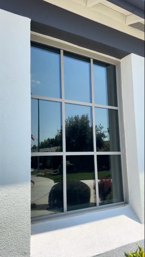 Residential window with reflective tint on a white stucco home exterior